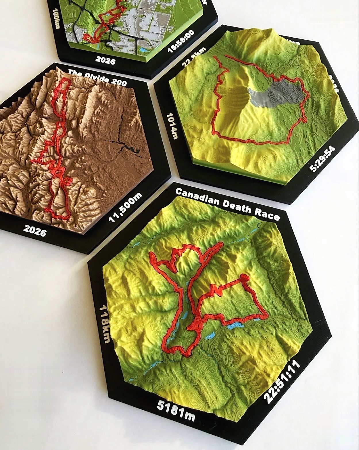 Canadian Death Race tile reading 118 km, 5181 m and 22:51:11, next to The Divide 200 tile printed in brown desert tones.